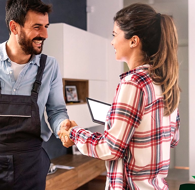 A technician in overalls shaking hands with a homeowner in a living room