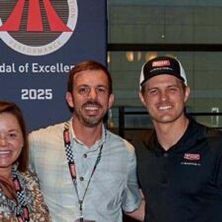 Three members of the Dinomite team in front of a Bryant Medal of Excellence 2025 banner